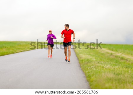 Man and woman two people runners running on country road, healthy fitness lifestyle, sport speed training beautiful landscape. Young couple doing workout exercising walking outdoors in nature.