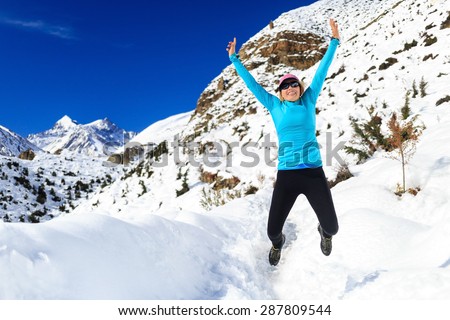 Happy woman jumping and cross country trail running in beautiful inspiring mountains landscape. Healthy lifestyle, fitness and exercising outdoors in winter nature. Inspiration and motivation.