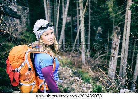 Woman hiking and camping on trail in winter dark dry forest. Recreation and healthy fitness lifestyle outdoors in inspirational nature. Beauty blond hiker camp with backpack looking at camera.