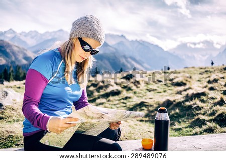 Young woman hiker reading and checking map in mountains on hiking trip. Healthy lifestyle fitness girl camping, drinking coffee and looking at beautiful inspirational landscape view in Tatras, Poland.