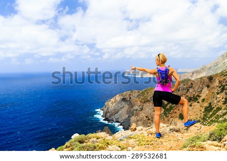 Woman cross country running or hiking, pointing hand at ocean, looking at beautiful inspirational scenic view in mountains and blue sea. Climbing or trail running healthy lifestyle in Crete, Greece