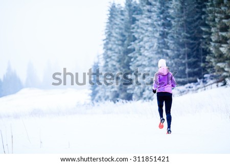 Sport, fitness inspiration and motivation. Young happy woman cross country running in mountains on snow, winter day. Female trail runner jogging exercising outdoors.