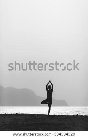 Woman meditating in yoga vrksasana pose silhouette at the ocean, beach and mountains. Motivation and inspirational exercising. Healthy lifestyle outdoors in nature, fitness concept.
