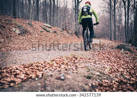 Mountain biker on cycle trail in woods. Mountains in winter or autumn landscape forest. Man cycling MTB on rural country road. Sport fitness motivation and inspiration.