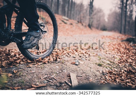 Mountain biker on cycle trail in woods. Mountains in winter or autumn landscape forest. Man cycling MTB on rural country road. Sport fitness motivation and inspiration. Selective focus on pedal.