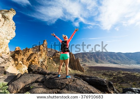 Woman hiker with arms outstretched in mountains. Beauty female runner, hands up and enjoy inspirational landscape on rocky trail footpath on Tenerife, Canary Islands