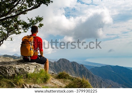 Man tourist hiker or trail runner looking at beautiful inspirational landscape in high mountains. Male runner with backpack, happiness and enjoying inspiring view on rocky top of mountain, Italy.