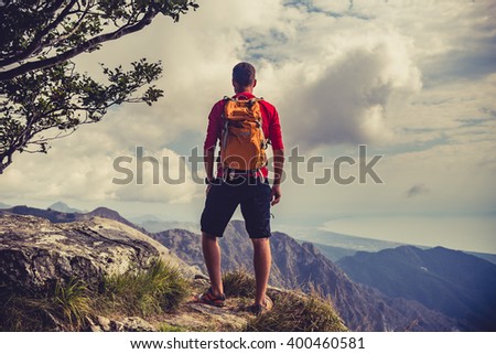 Hiking man, climber or trail runner in mountains, inspirational landscape. Motivated hiker with backpack looking at beautiful view. Trekking, travel and tourism concept. Fitness and healthy lifestyle.