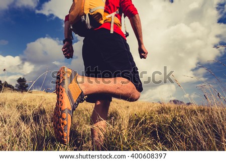 Hiking man or trail runner walking in mountain inspirational landscape. Fitness lifestyle hiker trekker walk in grass, fall autumn nature. Travel in Italy, Europe. Selective focus on a sports shoe.