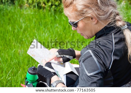 Woman on bicycle trip checking a map, adventure cycling in summer nature