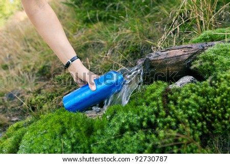 Woman taking water from mountain spring on hiking trip