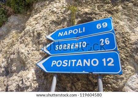 Napoli,Sorrento & Positano road sign indicating distances and the direction to take; against a rock face typical of Italian Amalfi Coast,listed as UNESCO World Heritage Site for its cultural landscape