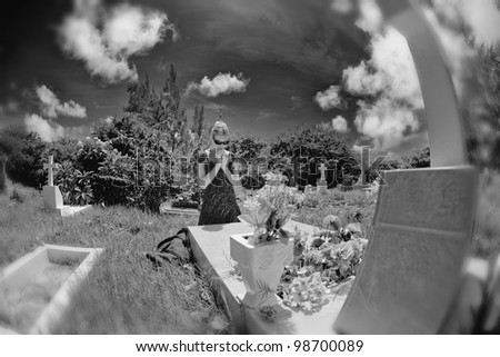 Mourning woman on her knees praying by a grave in a cemetery. Black and white, blur on borders