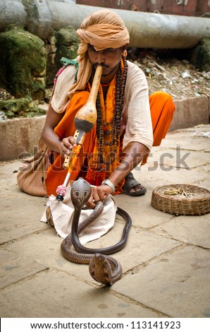 VARANASI, INDIA - AUGUST 6: snake charmer enchanting cobras in a street of Varanasi, India, august 6, 2012. People practice this dangerous job  as a way of begging charity