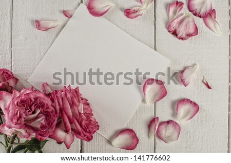 white paper on wooden  tabletop with rose petals and flowers