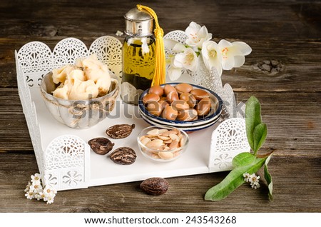 Still life of Argan oil and fruit and shea butter with nuts on a wooden table with flowers