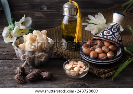 Still life of Argan oil and fruit and shea butter with nuts on a wooden table with flowers