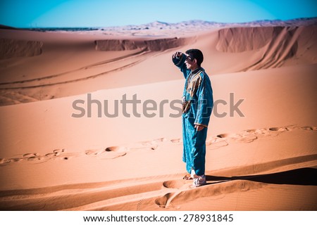 MERZOUGA, MOROCCO - 27 MARCH 2015: unidentified tuareg looking for something in the dunes of Sahara desert. Tuareg are called blue men for their traditional dresses