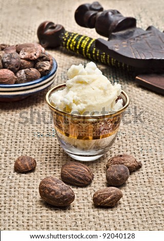 Still life with shea butter in a glass and shea nuts with african objects in the background