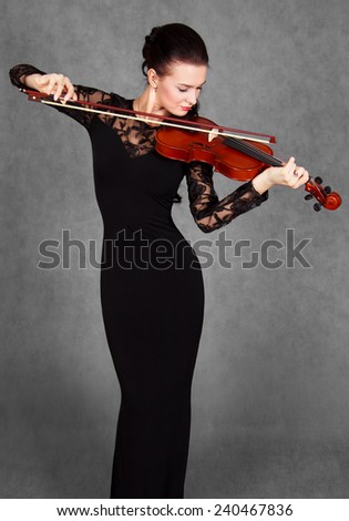 Portrait of a young attractive violinist woman in a black evening dress over grey background