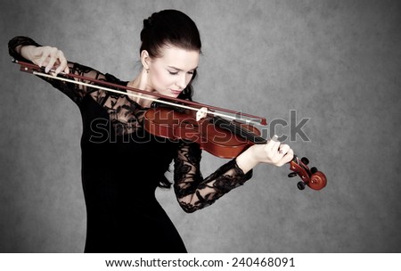Portrait of a young attractive violinist woman in a black evening dress over grey background