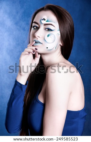 Portrait of a young attractive woman with a blue face art over dark blue background in cold colors