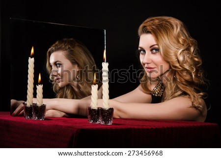 Beautiful young woman with candles near the mirror over black background