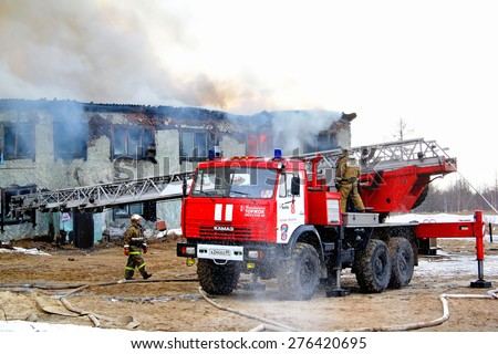 NOVYY URENGOY, RUSSIA - MAY 9, 2015: Modern fire ladder KAMAZ 43114 AL-30 near the burning old wooden residential house.