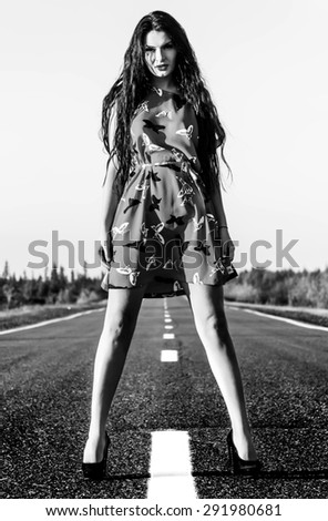 Black and white photo of a sexy young woman staying on the road