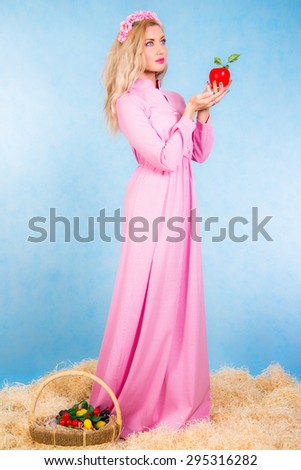 Beautiful young blonde in a long pink dress staying in a hay over cyan background