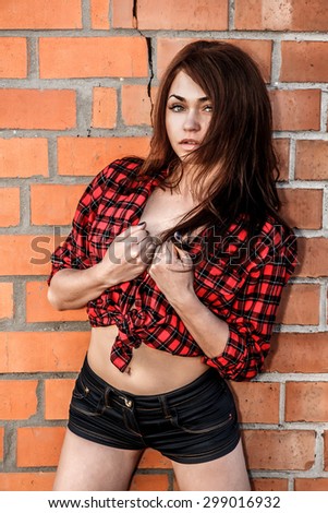 Beautiful young woman in a checked shirt at the background of the brick wall