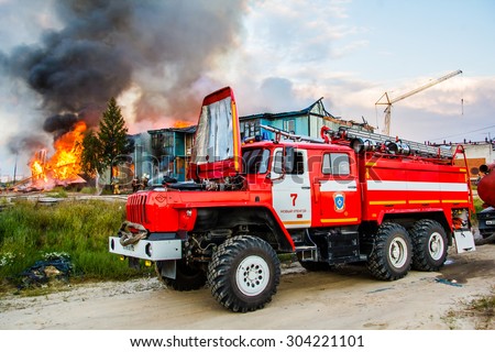 NOVYY URENGOY, RUSSIA - AUGUST 3, 2015: Red firetruck Ural 5557 takes part in the extinguishing of a fire in an old wooden house.