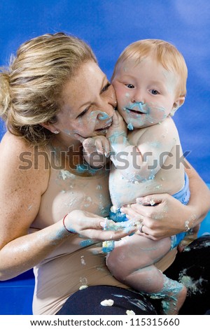 Baby's first birthday cake smash party. A baby boy playfully covering him and his mother in birthday cake.