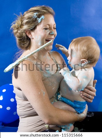 Baby\'s first birthday cake smash party. A baby boy playfully covering him and his mother in birthday cake.