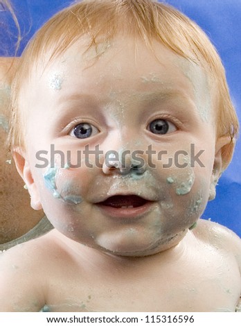 Blue eyed boy smiling with cake covering his face. Baby\'s first birthday cake smash party.