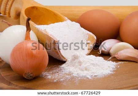 Onions, eggs, garlic, flour, scoop on a wooden pastry board