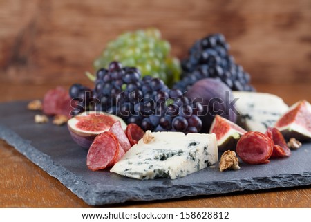 Slate board with blue cheese, blue and green grapes, figs, walnuts and salami