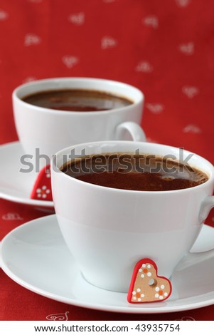 Caps of coffee with little ceramic hearts on red background. Shallow dof, copy space
