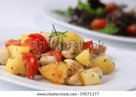 Fried potatoes with mushrooms and cherry tomatoes garnished with chives and sesame seeds. Shallow dof