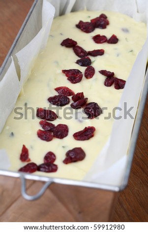 Cake tin with zucchini bread batter and dried cranberries ready to be put into the oven. Shallow dof