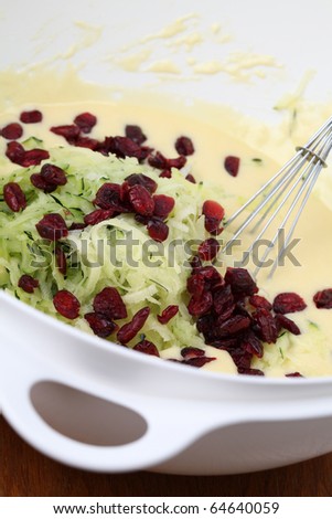 Bowl with batter, grated zucchini and dried cranberries for delicious zucchini bread. Shallow dof