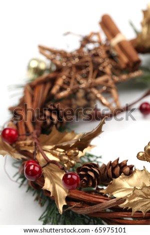 Christmas wreath with golden holly leaves, cones, red berries and cinnamon on white background. Shallow dof