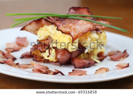 Scrambled eggs and bacon, garnished with chives on white plate