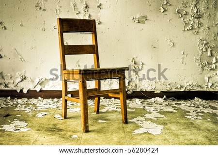 Image of an old wooden chair in an abandoned building with cracked and peeling paint illuminated by natural daylight.
