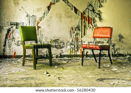 Image of old chairs in an abandoned building with cracked and peeling paint illuminated by natural daylight.