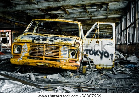 Image of a destroyed old, rusty truck covered in graffiti in an abandoned factory warehouse.