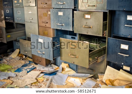 Image of old rusty filing cabinets in a derelict abandoned building with files scattered on the floor.