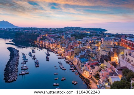 Serene sea, colorful houses on coastline, fishing and sightseeing boats in Marina Corricella in sunset time at Procida island, Italy. Procida is located between Capo Miseno and island of Ischia.