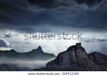 Nature background - dark stormy sky above mountains, fortress on top of rock