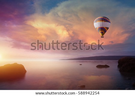 Amazing heavenly background - two colorful hot air balloons flies in glowing sunset sky above calm sea